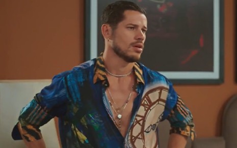 O ator José Loreto com expressão séria e camisa estampada, com peito de fora, em cena de Vai na Fé