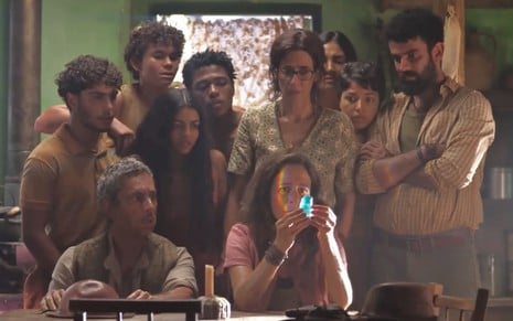 Zefa Leonel (Andrea Beltão) segura pedra preciosa azul na mão; toda a família está em volta dela na cena da novela No Rancho Fundo