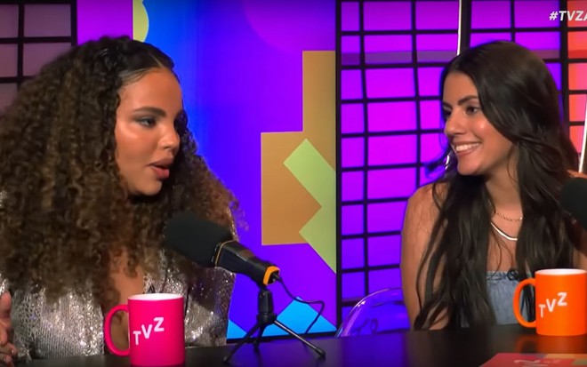 Giovanna Pitel e Fernanda Bande estão sentadas, em frente a dois microfones, dando entrevista ao TVZ