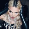 Madonna leva as duas mãos à cabeça em foto promocional; ela usa vestido preto e muitas joias