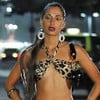A atriz Camila Pitanga caracterizada como Bebel, de top, brincos grandes e cabelo preso, em cena noturna na rua, em Paraíso Tropical